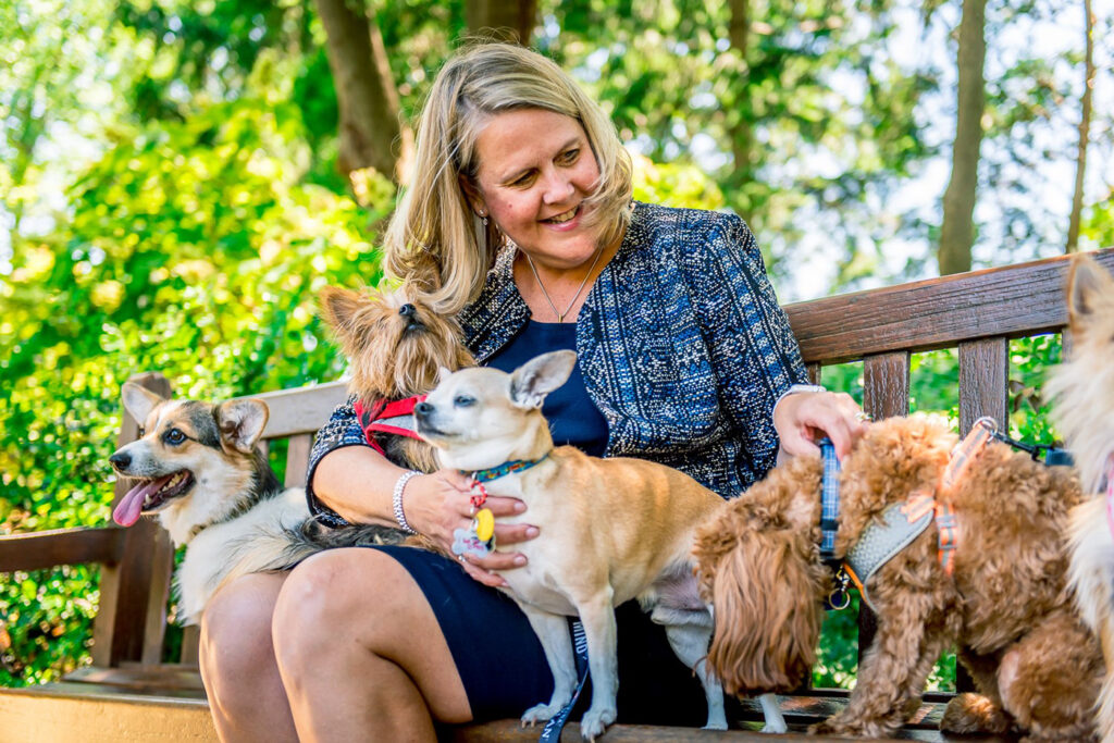 Color portrait of WashU alumna Nina Leigh Krueger posing with several dogs on a park bench