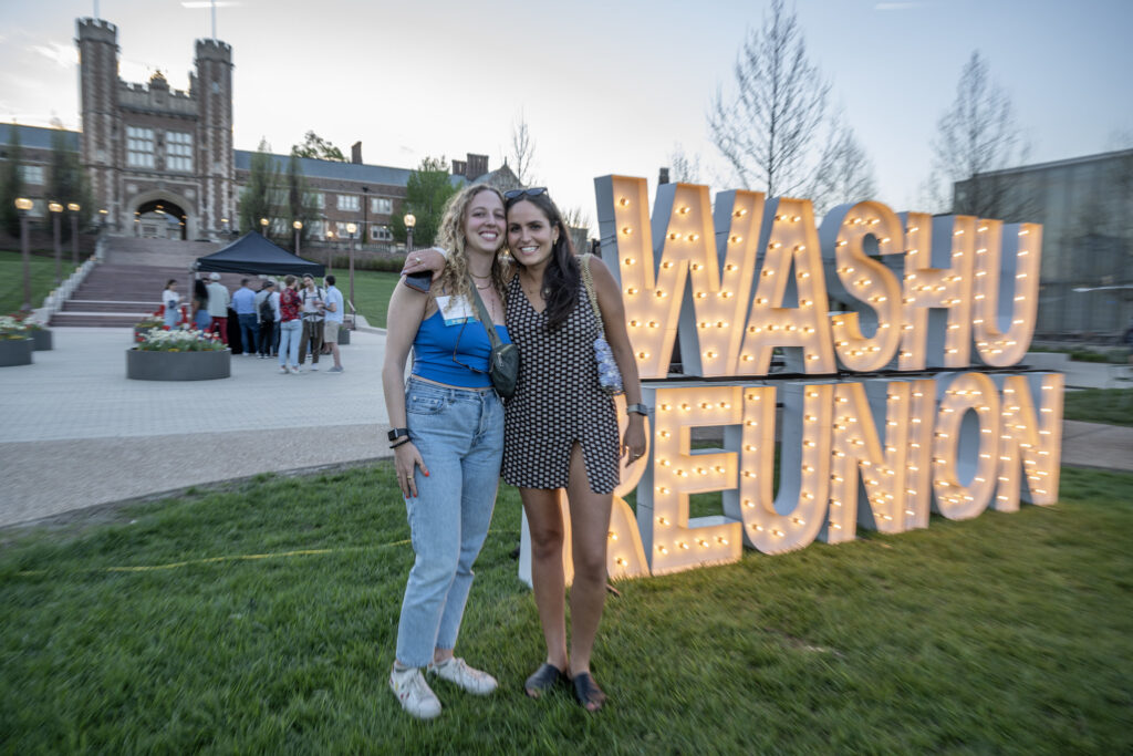 Two alumnae pose in front of a Reunion sign