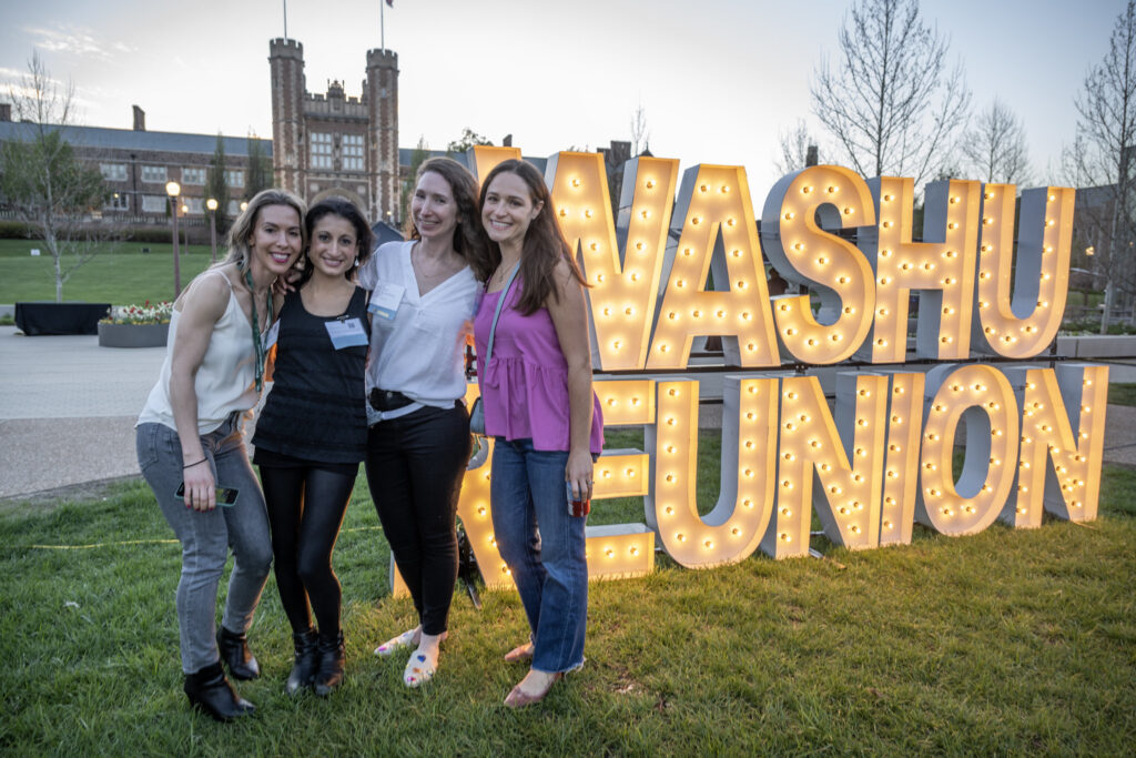 Four alumnae pose in front of a WashU Reunion sign