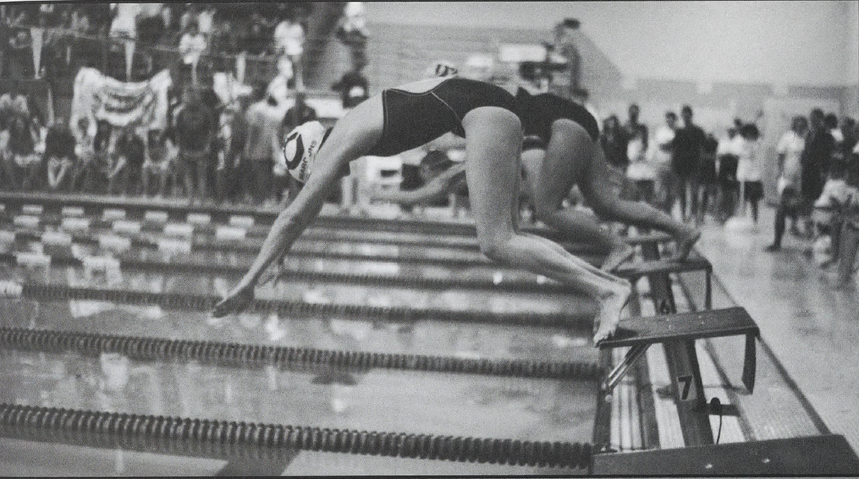 Black and white photo of female swimmers diving off starting blocks