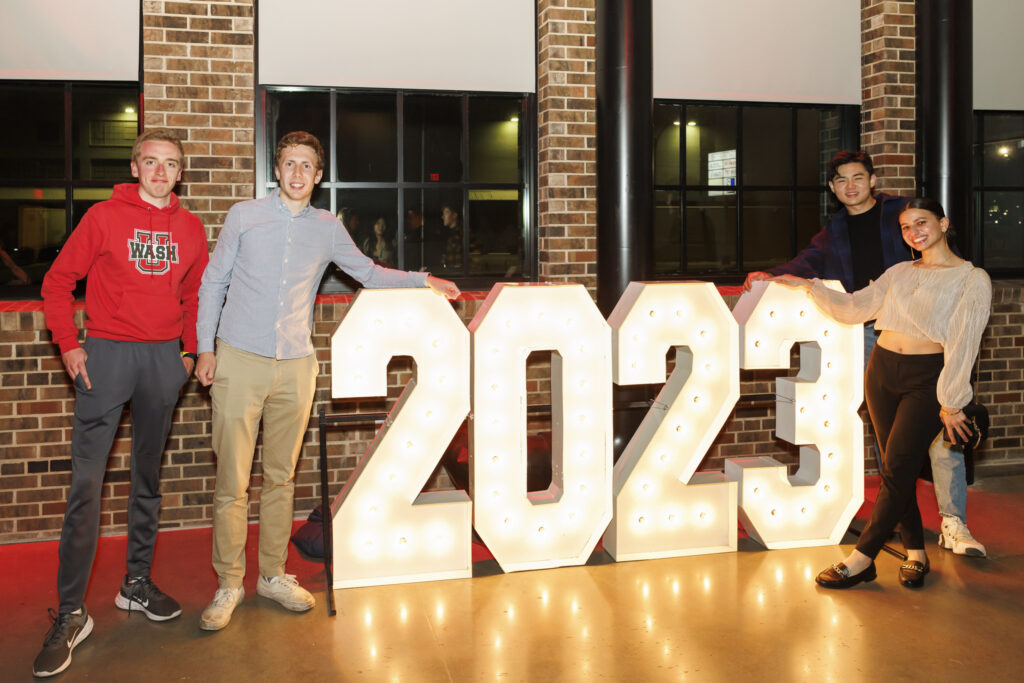 Four Class of 2023 alums take a photo next to the 2023 sign